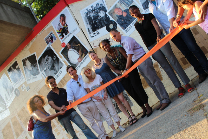 Group of people in front of the Mt. Hope Music Mural, cutting an orange ribbon at dedication ceremony.