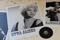 Black-and-white portrait of Etta James on textured wall, showing the singer looking to the side; a vinyl record and another musician photo nearby.